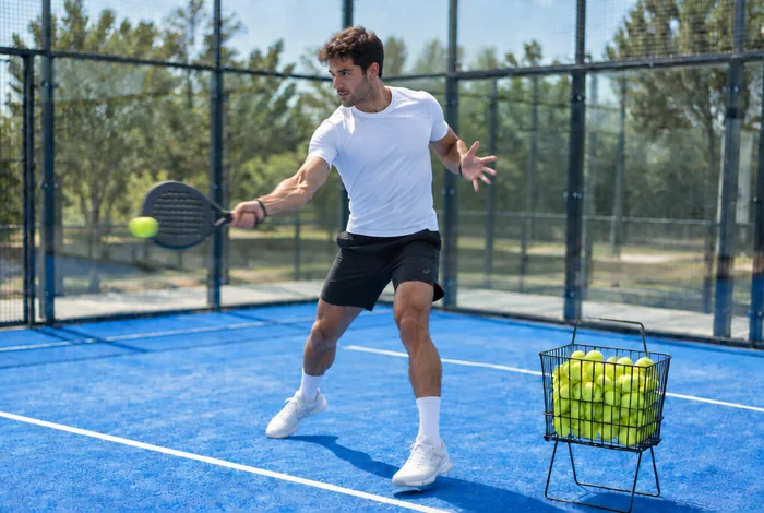Padelspeler slaat een forehand naast de ballenmand